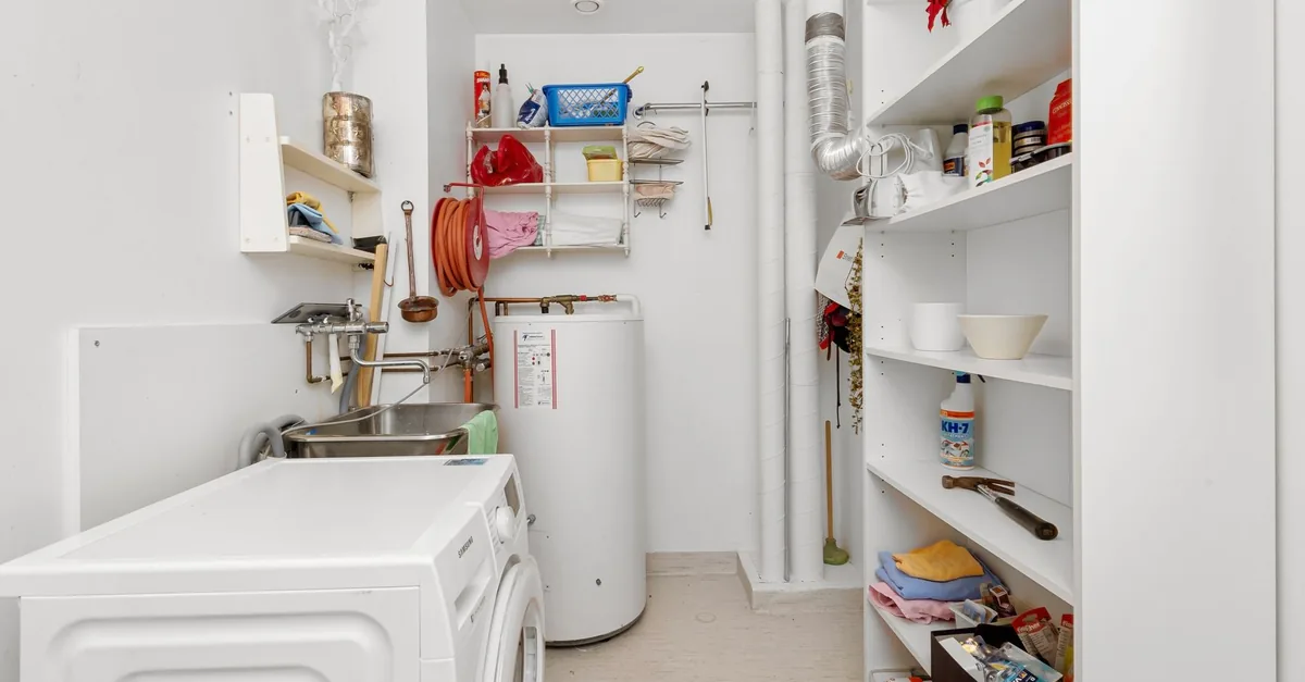 A white storage hot water cylinder beside a washing machine in a home laundry