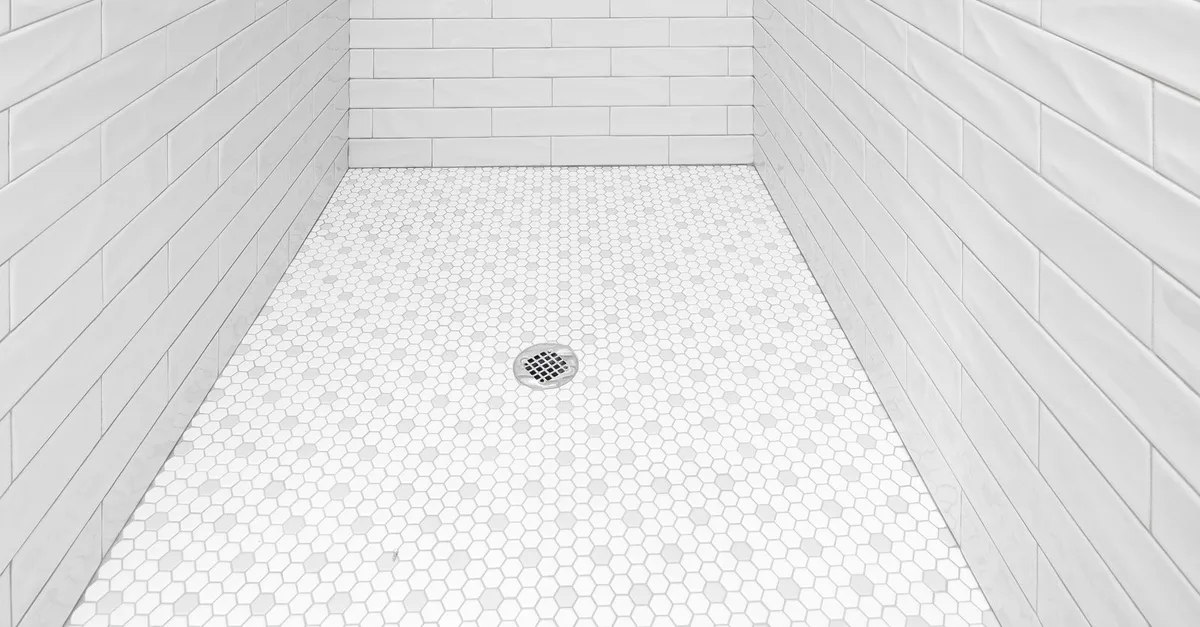 A white tiled shower recess with a chrome floor waste in the centre